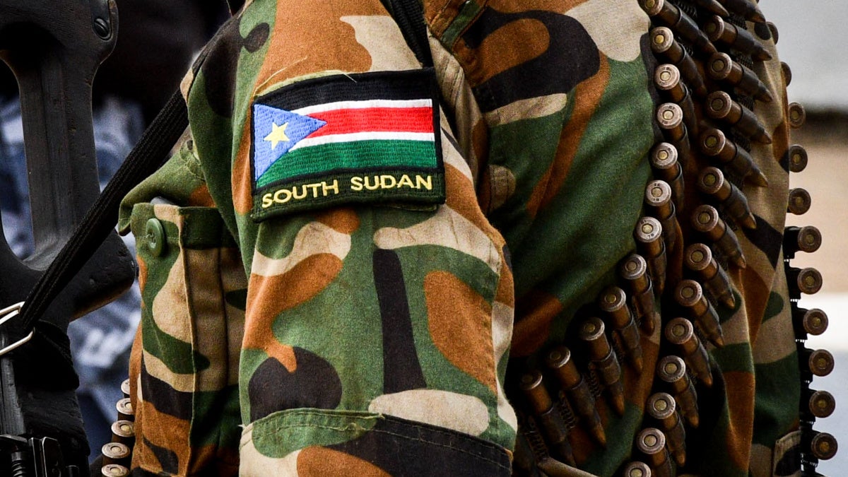 Illustrative close-up of a person in South Sudan military uniform with a flag patch and ammunition belt